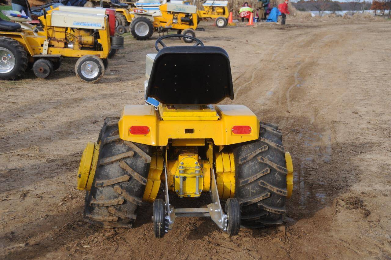 A yellow tractor parked in the dirt with other tractors behind it.